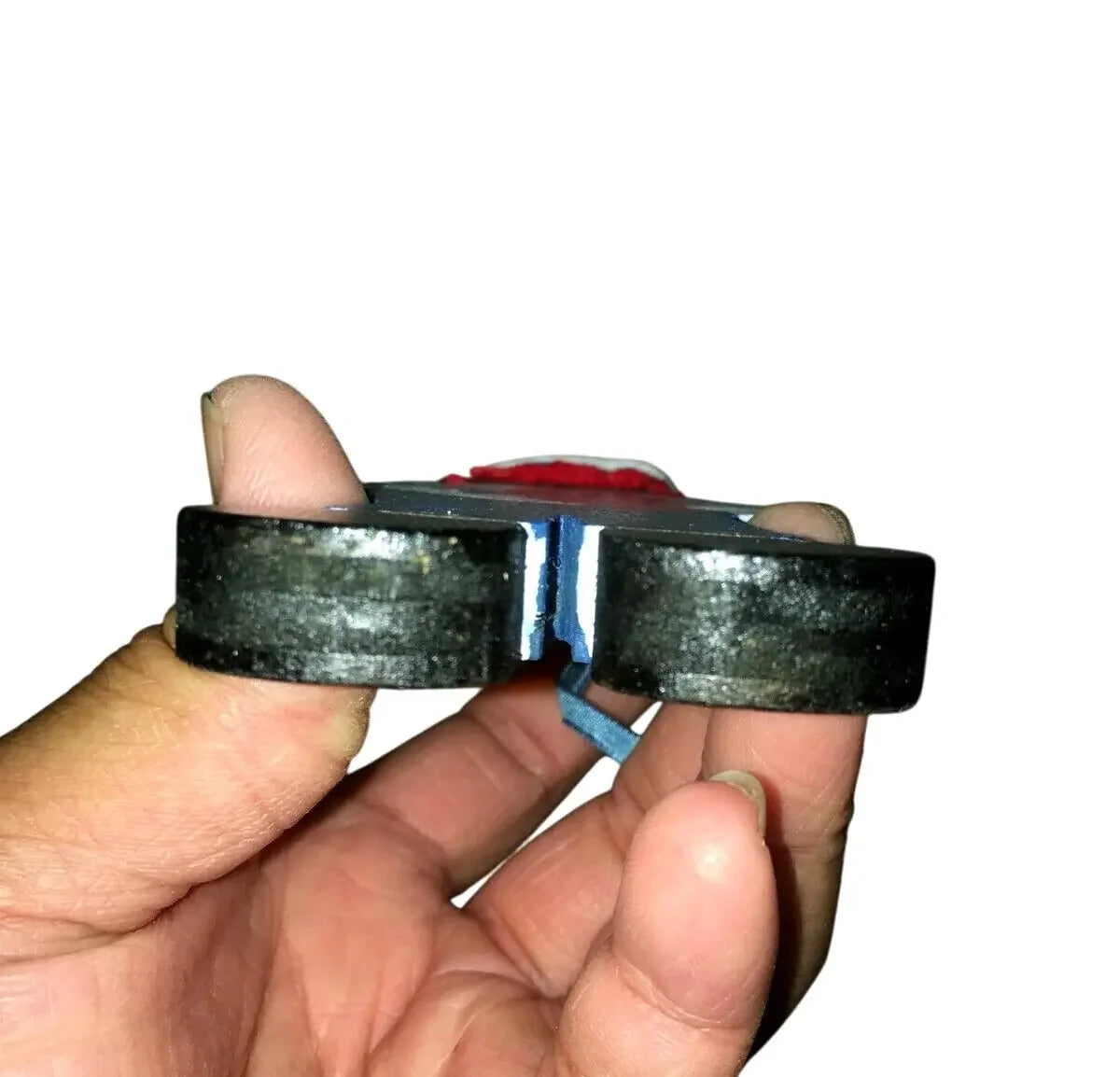 Hand holding a round metal magnet with a gap in the center, white background