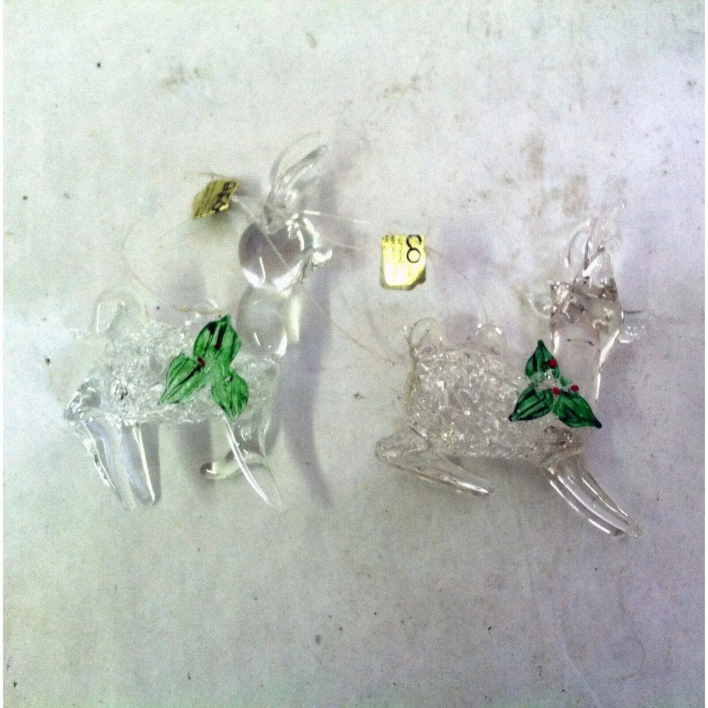 Clear glass reindeer ornaments with green holly leaves and red berries on a white background