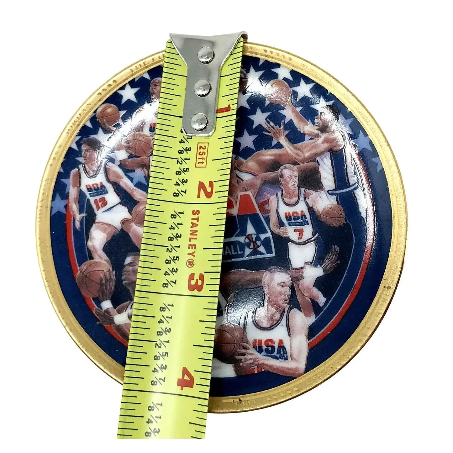 Round collectible plate with USA basketball players, gold rim, and tape measure across center