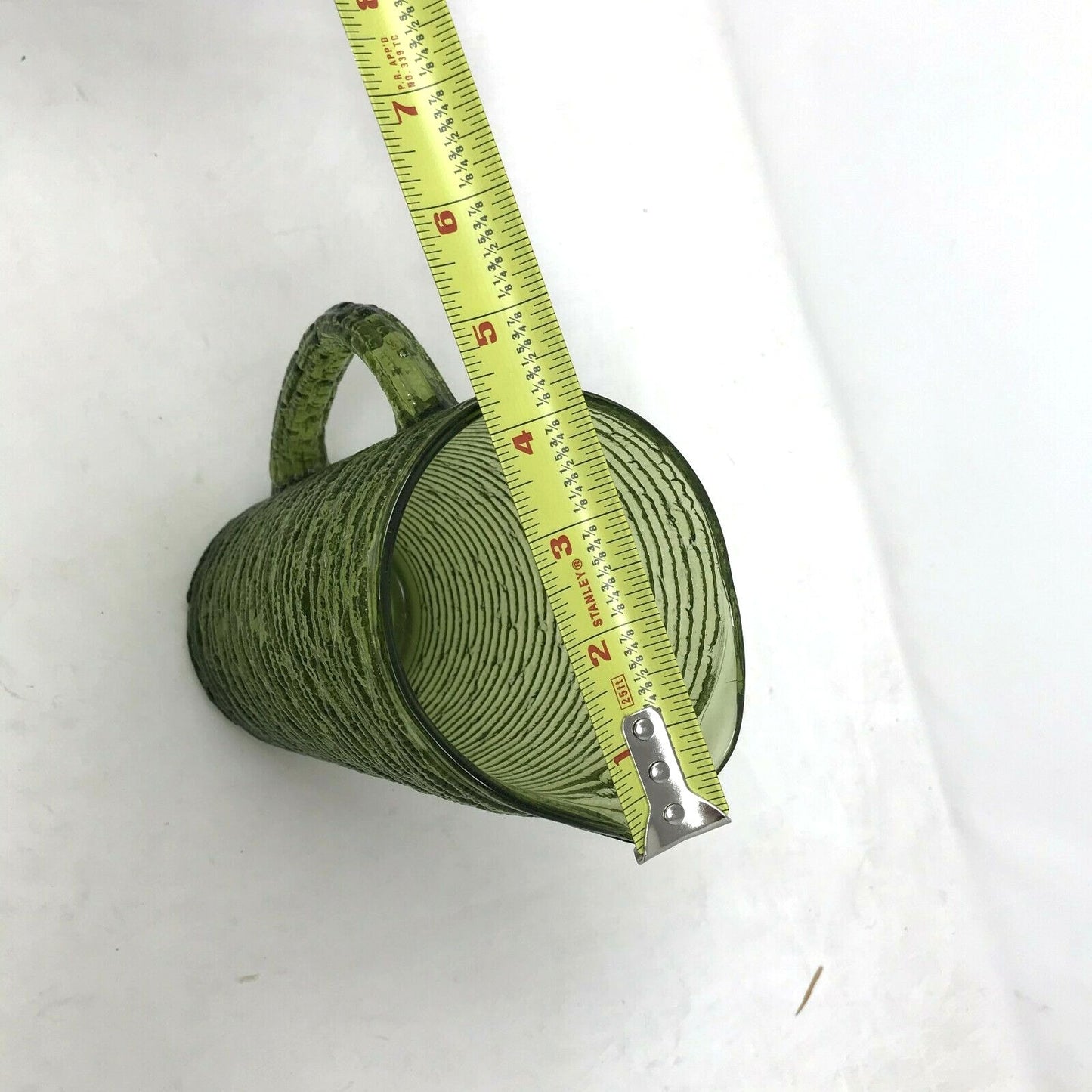Green textured glass mug measured with a yellow tape measure on white background
