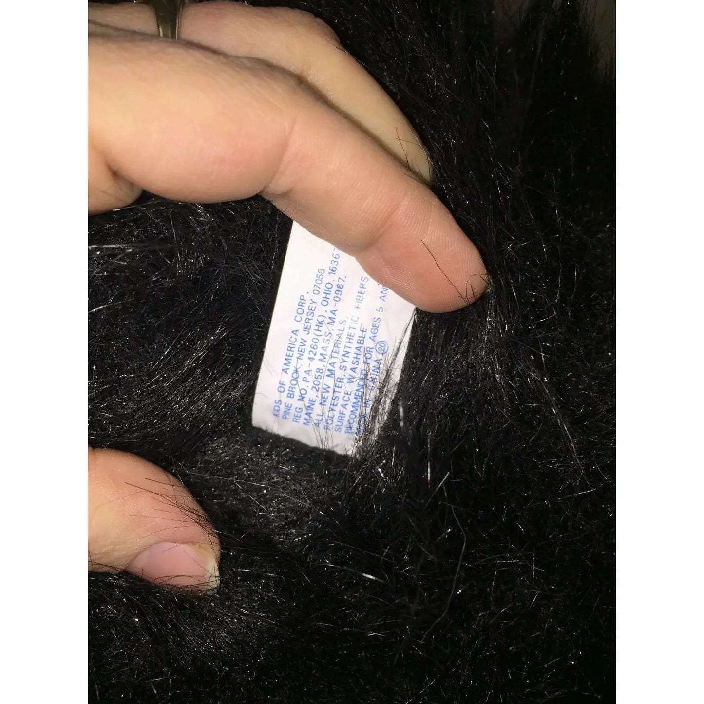Hand holding clothing care tag on black faux fur fabric, close-up texture detail
