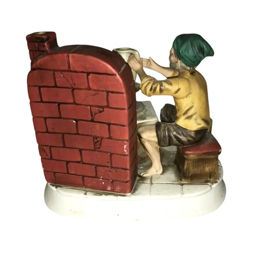Ceramic figurine of a person with green hat shaping pottery at a kiln with red brick wall