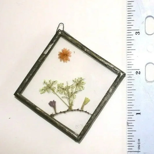 Pressed flower pendant in square glass frame beside ruler for size reference