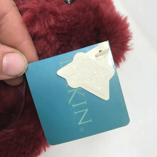 Hand holding burgundy plush toy with blue tag and embossed bear-shaped label