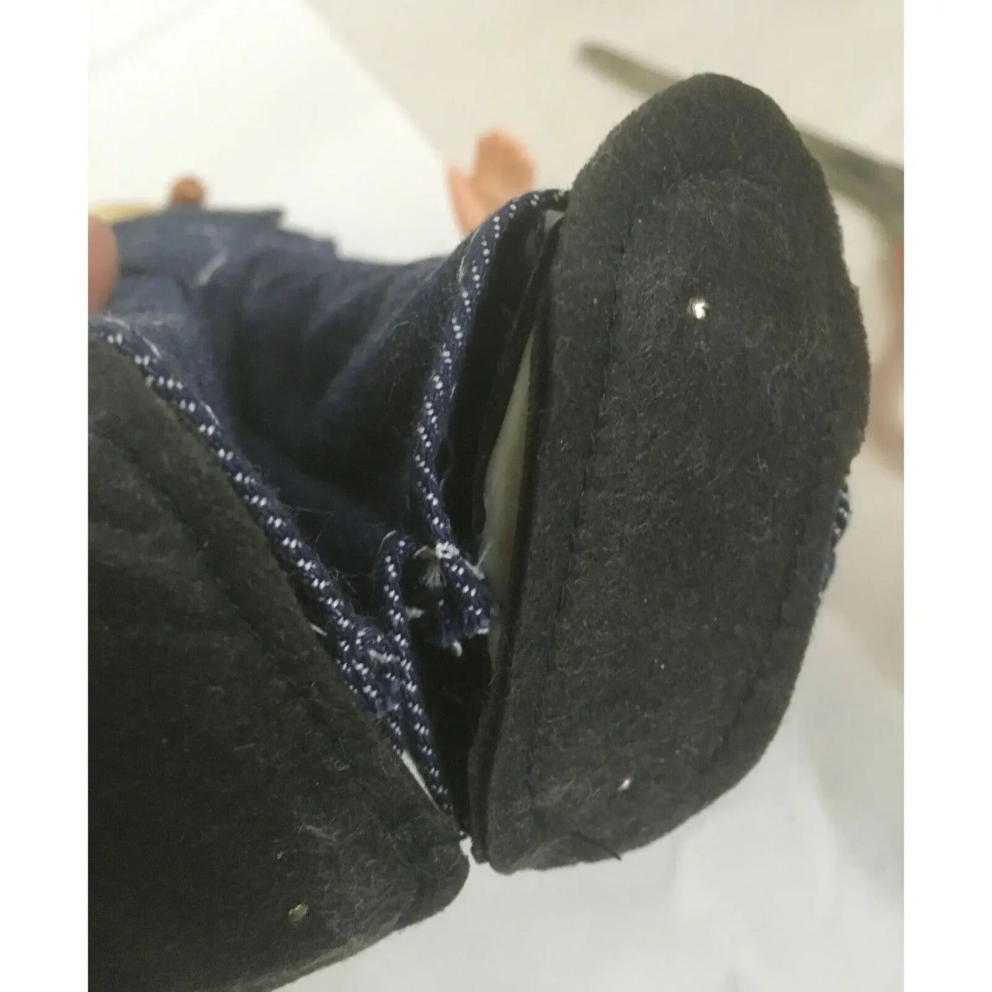 Close-up of a doll shoe with black sole and denim pants, showing stitching details