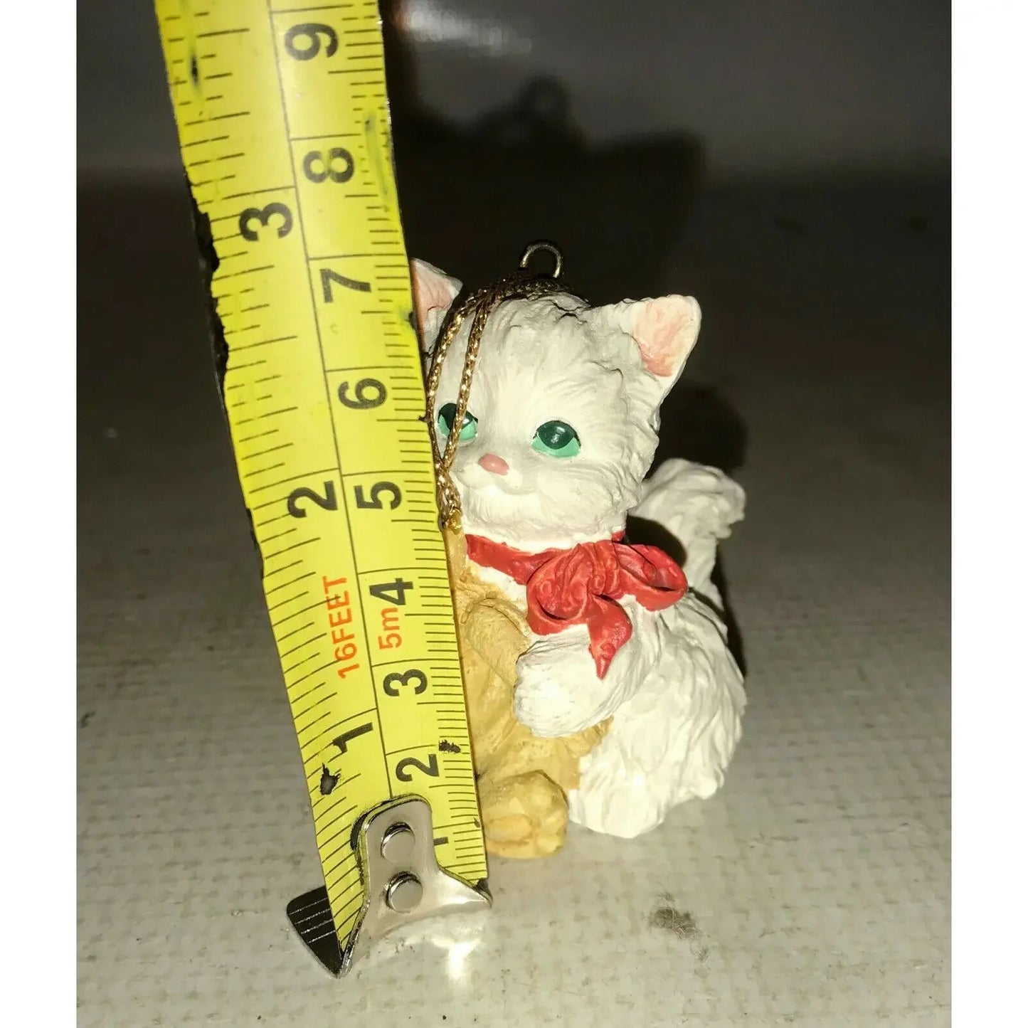 Small white cat figurine ornament with red bow, next to a measuring tape showing 2.5 inches tall
