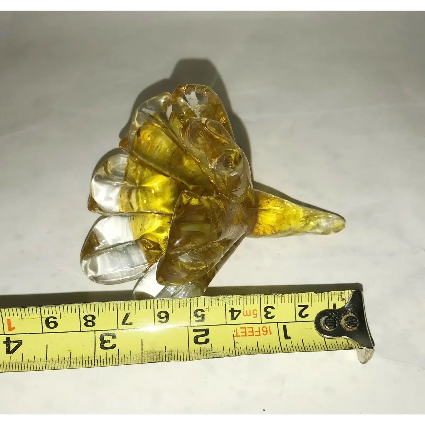 Yellow glass flower figurine next to a measuring tape on a white surface