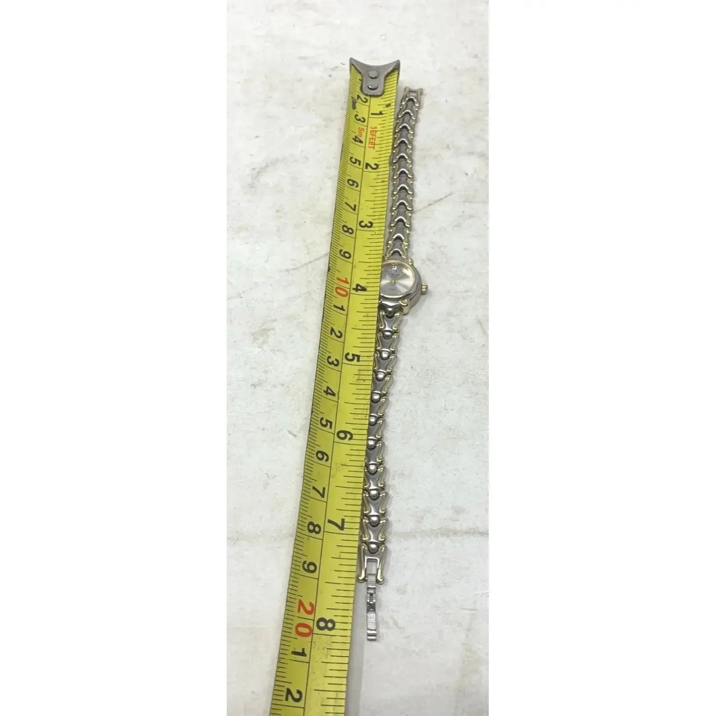Silver metal wristwatch next to yellow tape measure on light surface