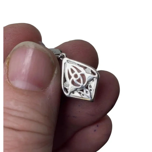 Hand holding a silver Celtic knot pendant with geometric design, jewelry on white background