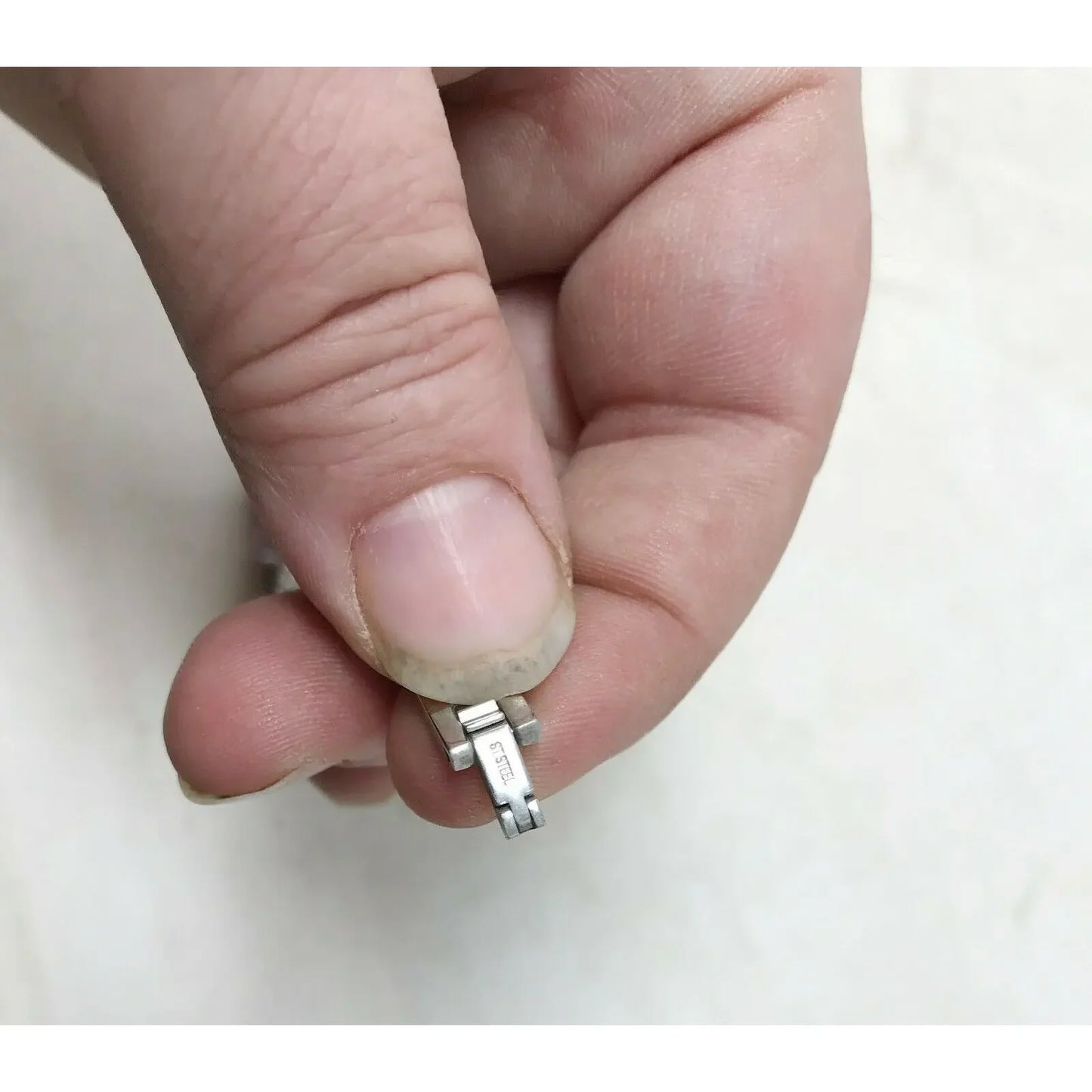 Hand holding a small stainless steel watch band clasp on a light background