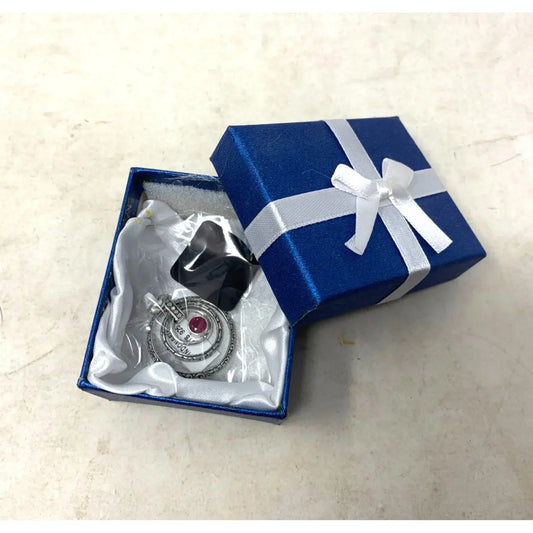 Silver pendant with red gem in blue gift box with white ribbon on light background