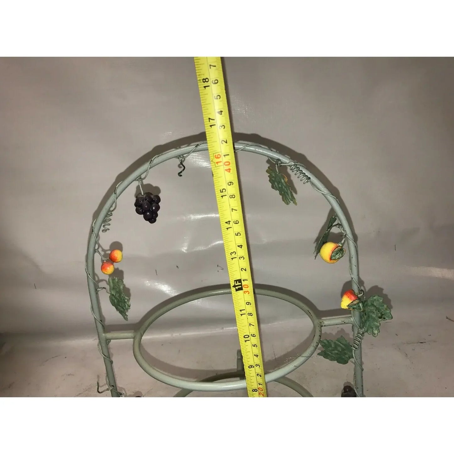 Metal fruit-themed rack with grape and peach decorations, measured with yellow tape