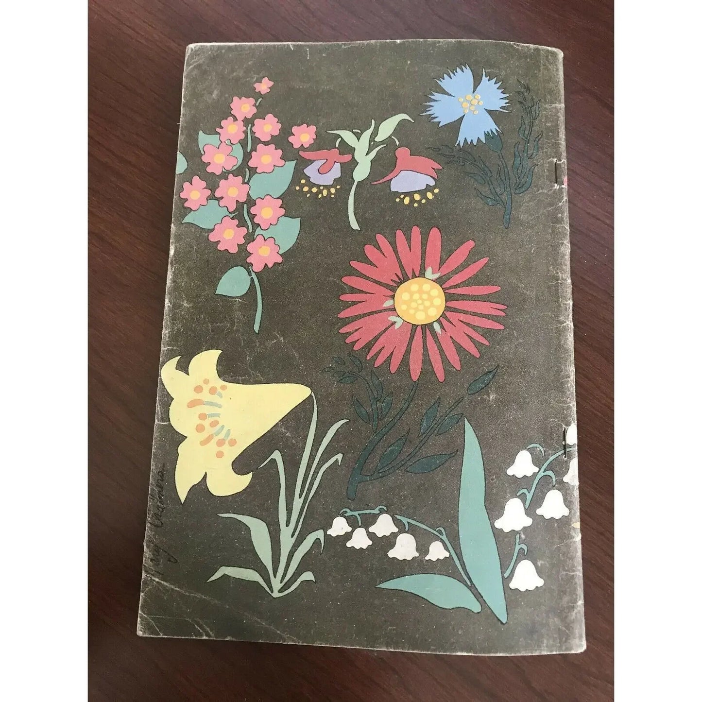 Vintage notebook with colorful illustrated flowers on a dark brown cover, placed on a wooden surface