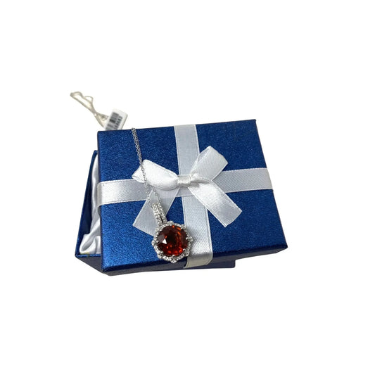 Silver necklace with red gemstone pendant on blue gift box with white ribbon