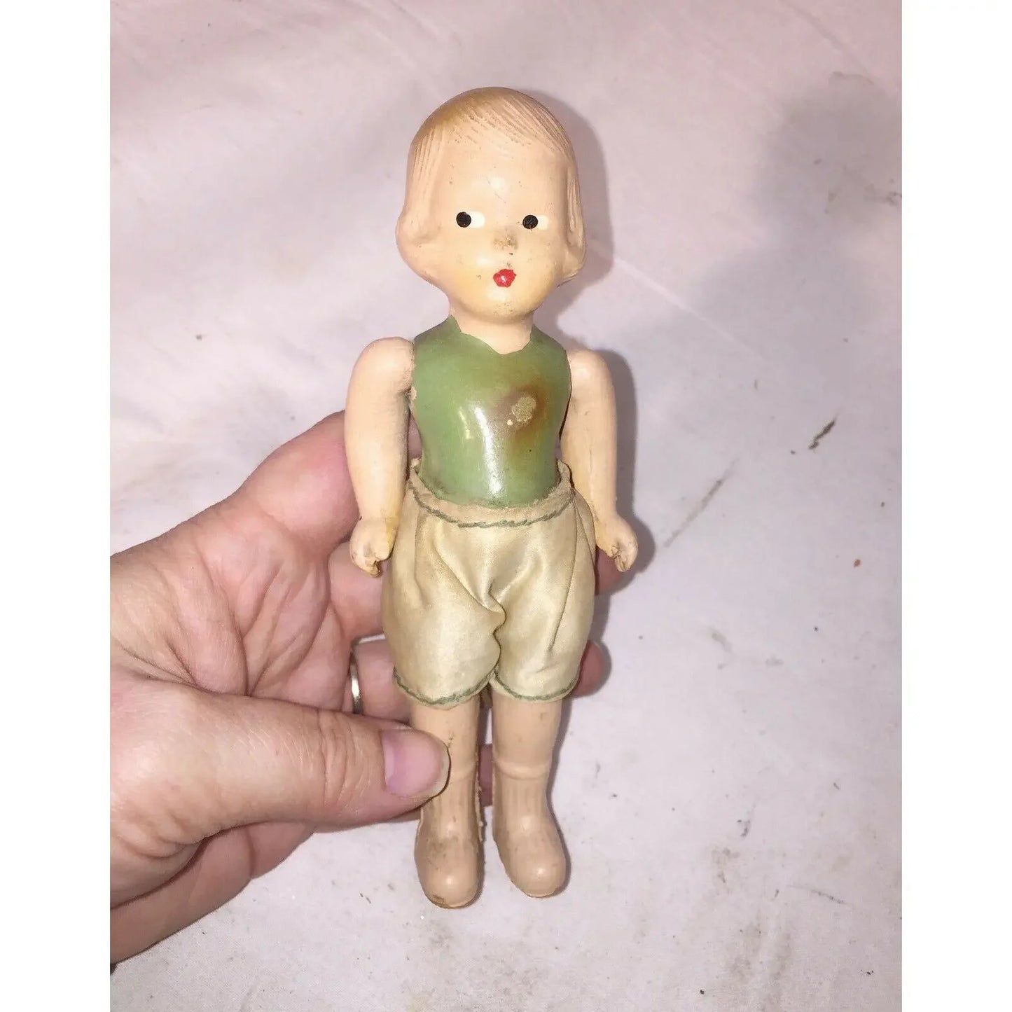 Vintage bisque doll with green top, beige shorts, and short blonde hair held in hand