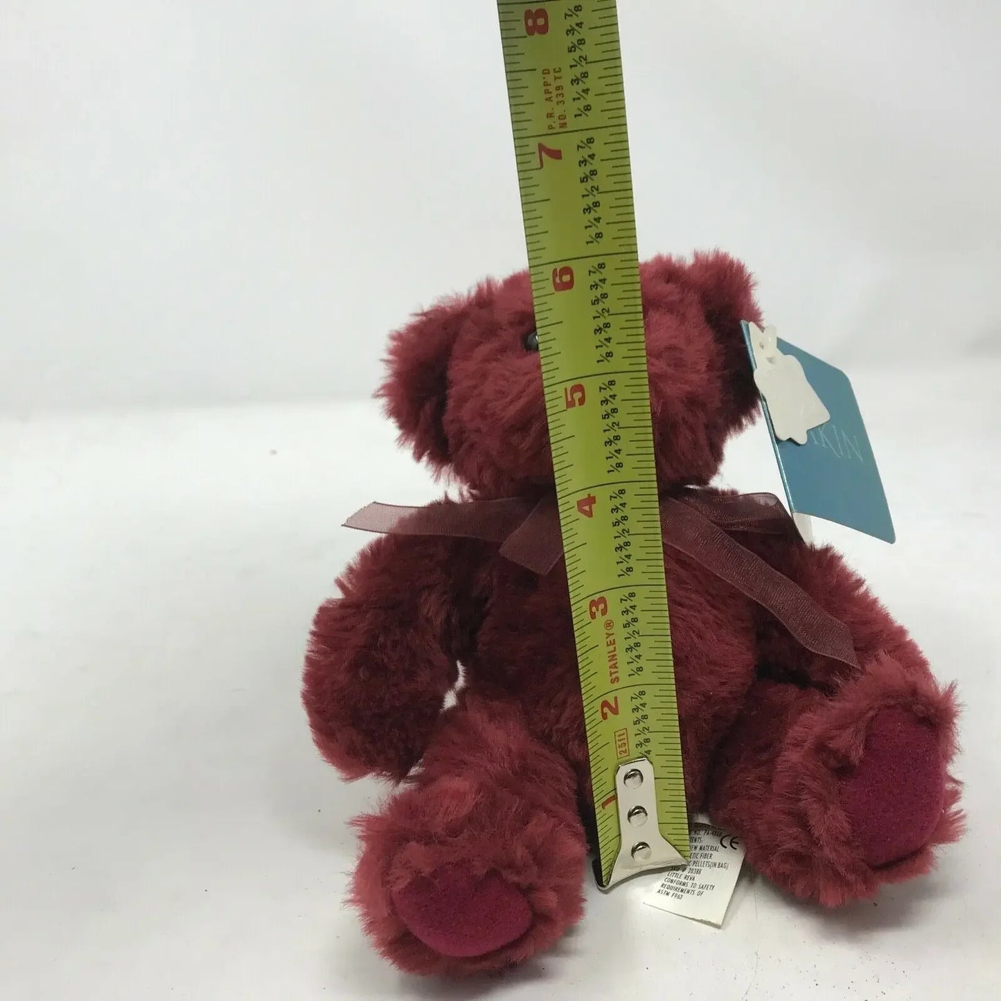 Plush burgundy teddy bear with ribbon, measured at 7 inches tall with tape measure