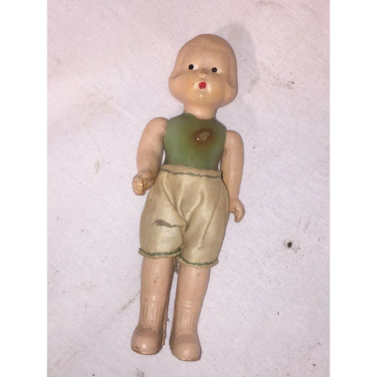 Vintage plastic doll with green shirt and beige shorts on white fabric background