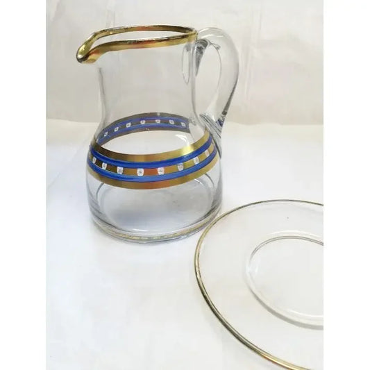 Clear glass pitcher with gold and blue band design, matching glass saucer beside it.