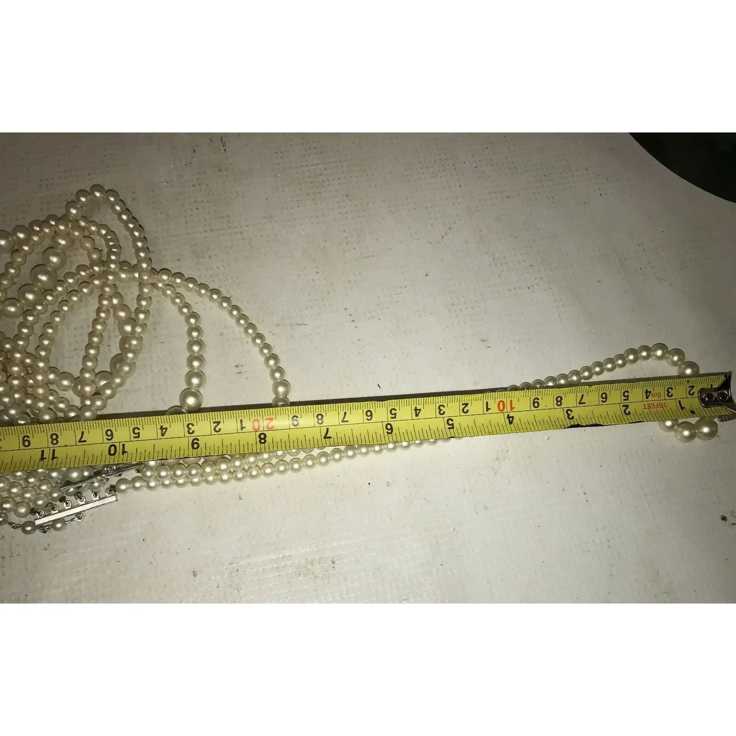 Pearl necklace with silver clasp measured by yellow tape measure on white surface