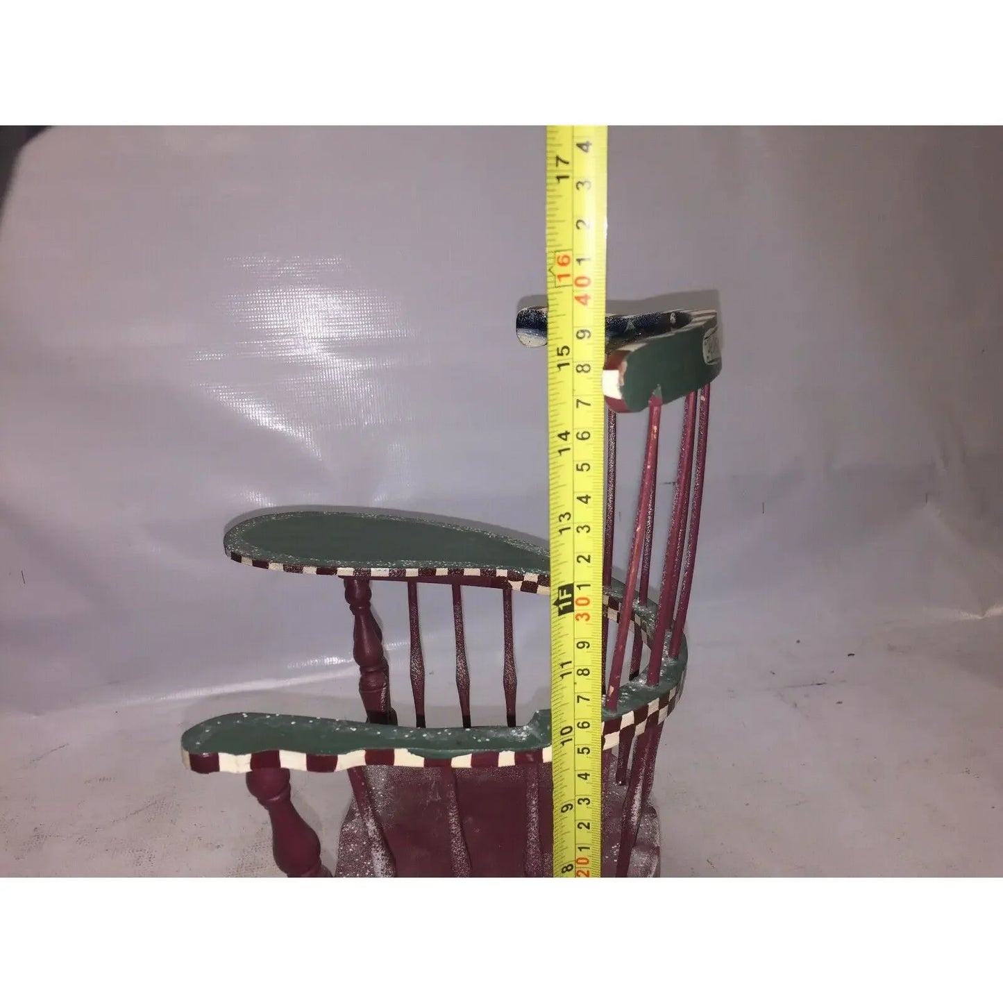 Red and green wooden miniature chair with measuring tape showing height