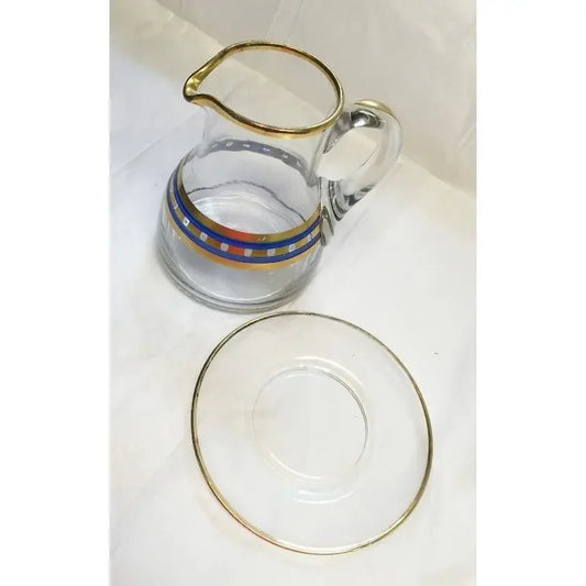 Clear glass pitcher with gold rim and colorful geometric band, paired with matching glass saucer