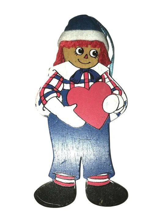 Wooden doll ornament with red yarn hair, plaid shirt, blue pants, holding a pink heart