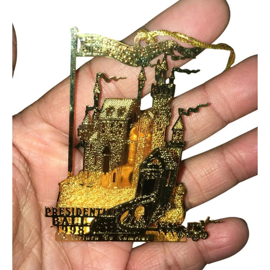 Hand holding gold castle ornament with detailed towers, flags, and engraved text.