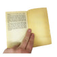 Hand holding open a small, vintage paperback book with yellowed pages and text visible.