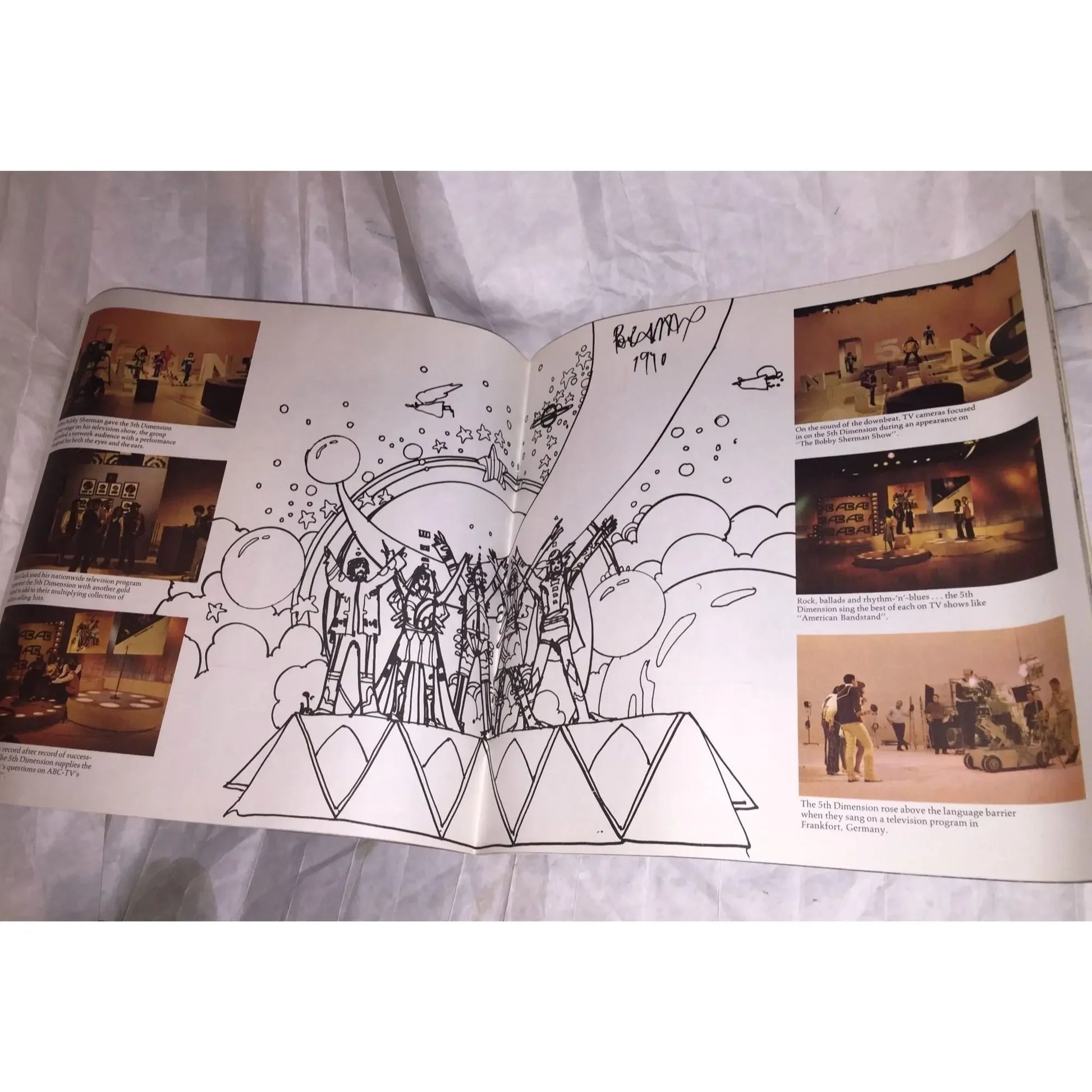Open magazine with black and white illustration and color photos of a musical TV show on a fabric surface.