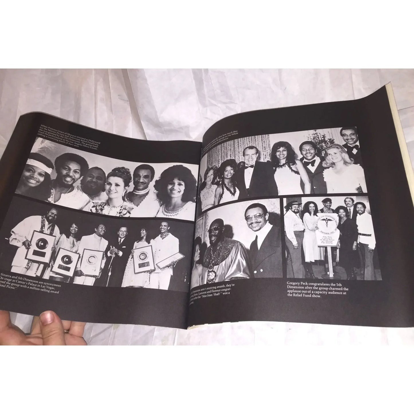 Open book displaying black and white photos of award ceremonies and group portraits on a white cloth.