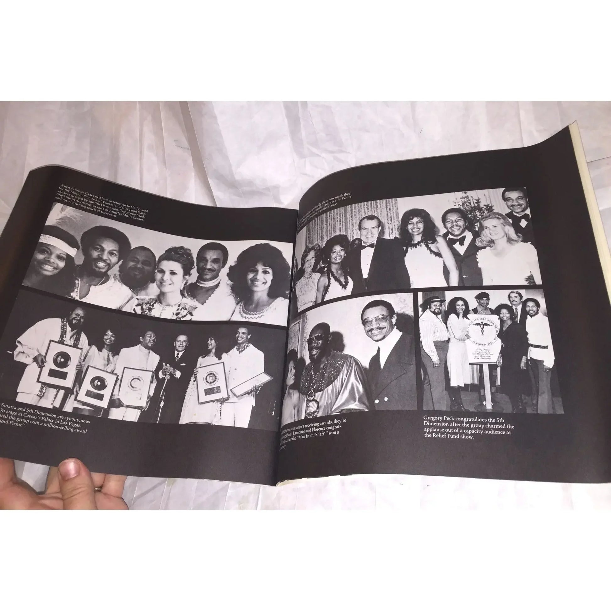 Open book displaying black and white photos of award ceremonies and group portraits on a white cloth.