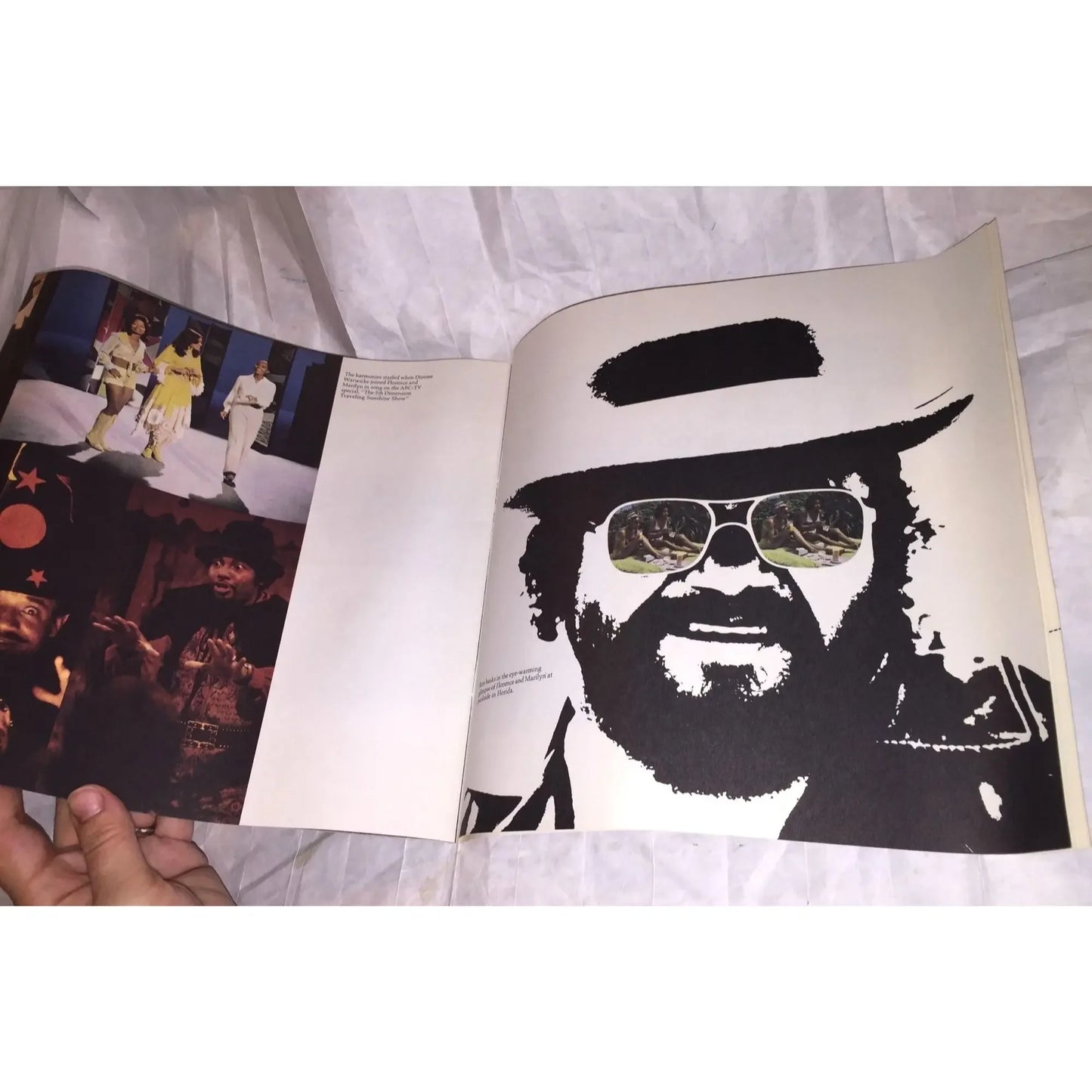 Open vintage photo book showing colorful performance images and a bold black-and-white portrait illustration of a man in sunglasses and a hat.
