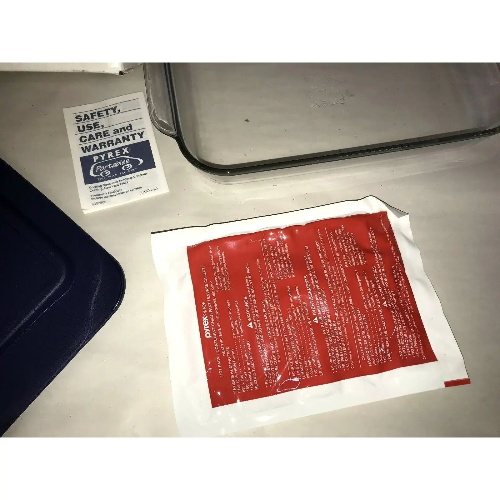 Pyrex glass baking dish with blue lid, red heat pack, and instruction manual on table