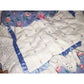 Close-up of a quilted fabric with floral patterns, lace trim, and a pink ribbon rose accent.