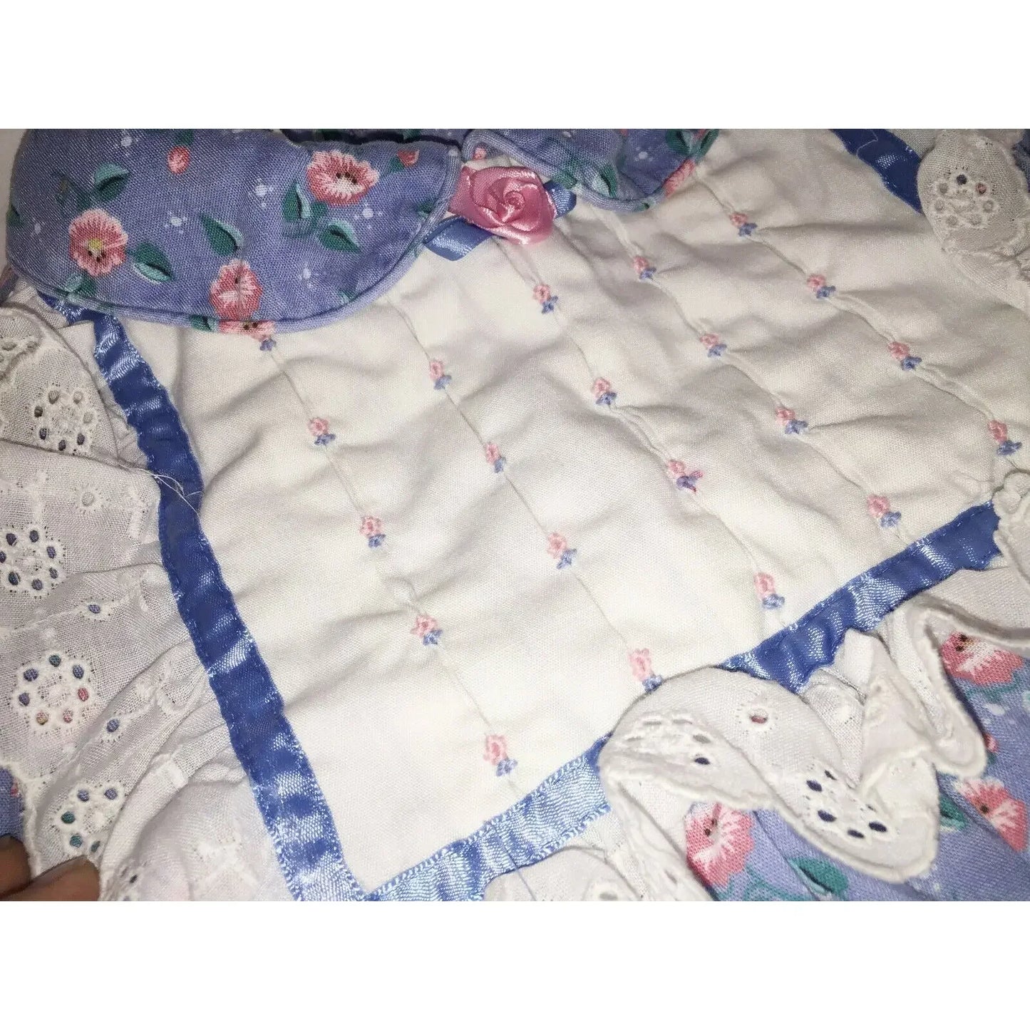 Close-up of a quilted fabric with floral patterns, lace trim, and a pink ribbon rose accent.