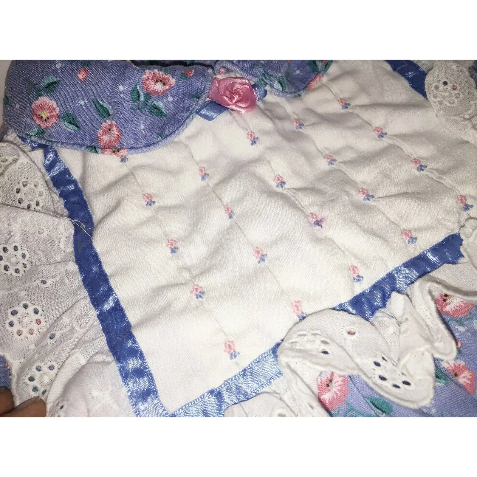 Close-up of a quilted fabric with floral patterns, lace trim, and a pink ribbon rose accent.