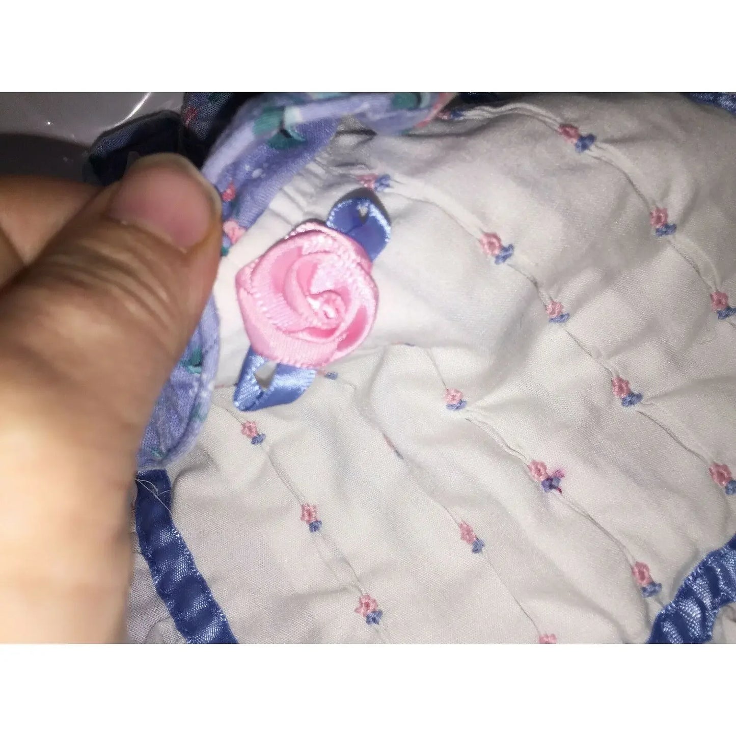 Hand holding quilted fabric with pink ribbon rose and blue floral trim