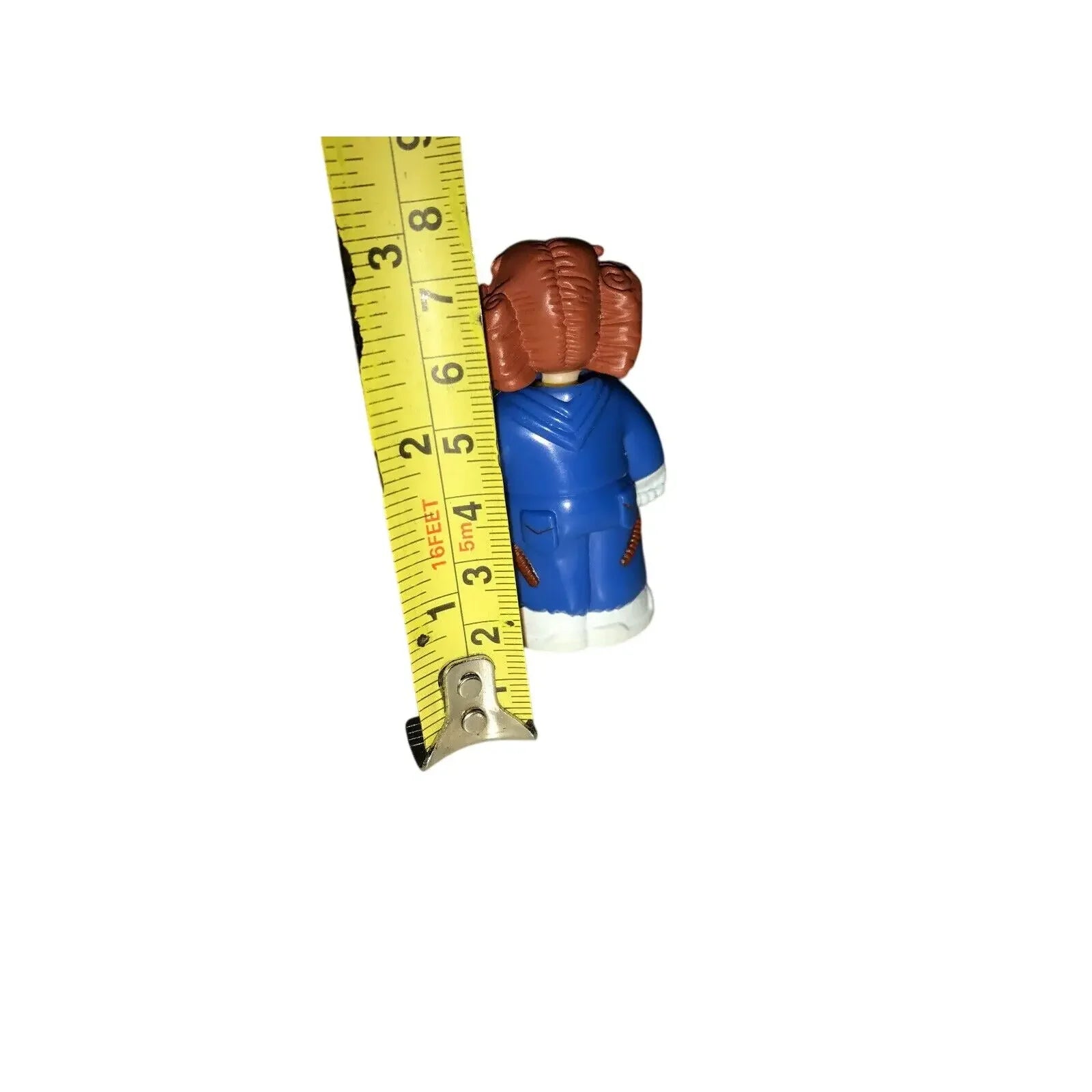 Small toy figure in blue outfit beside measuring tape showing height