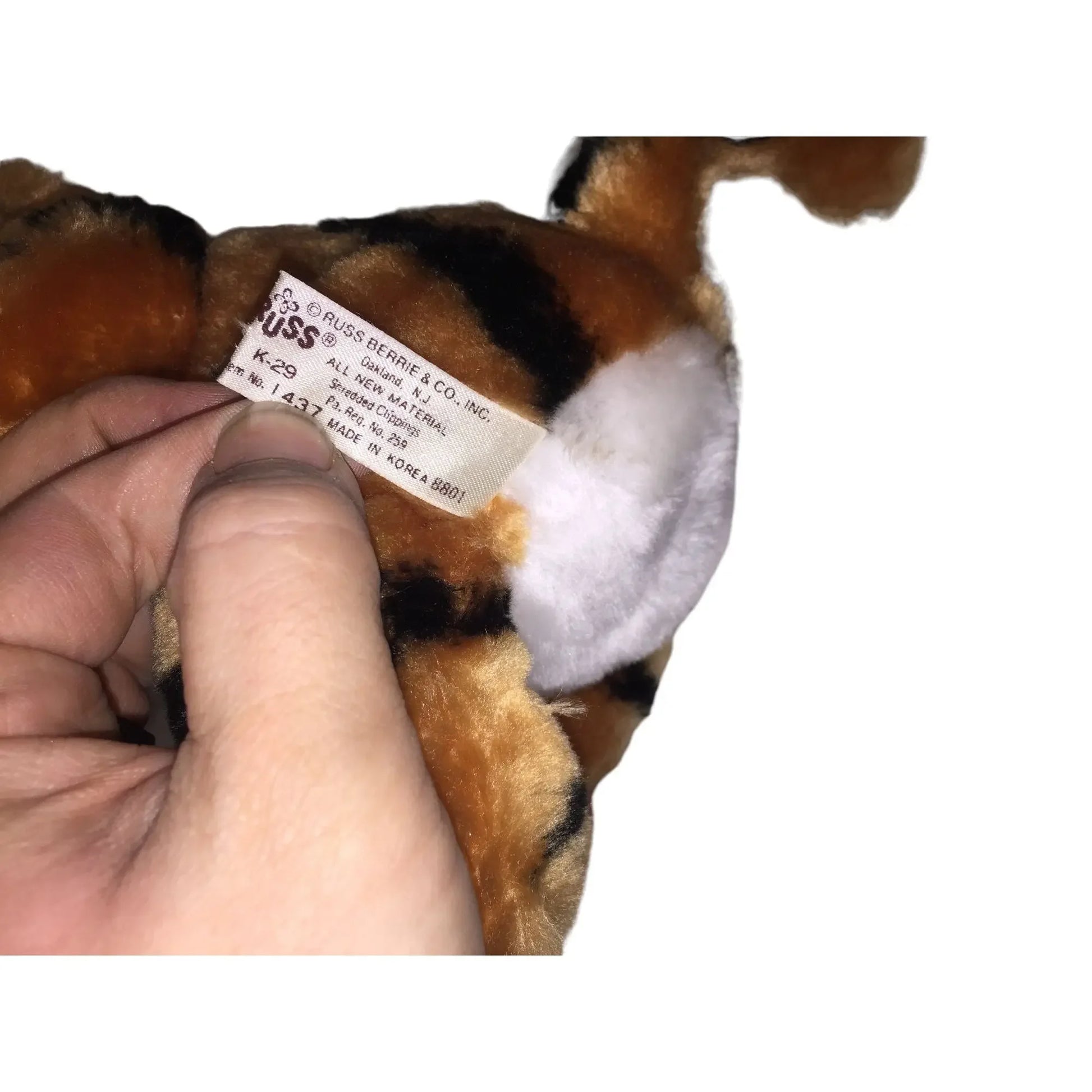 Hand holding plush toy with spotted fur and visible product label tag