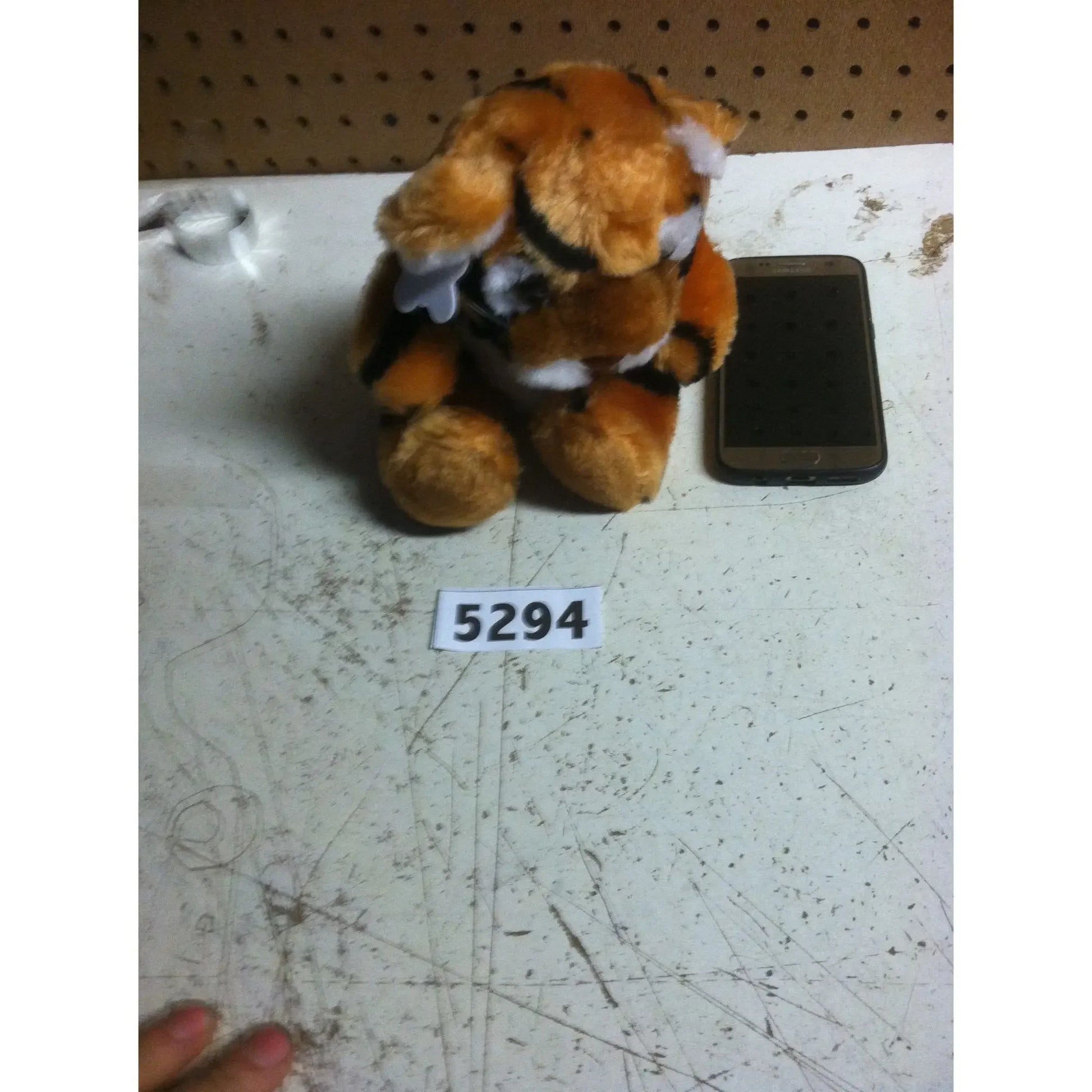 Plush tiger toy with white patches beside a smartphone on a scratched white table, tagged 5294.