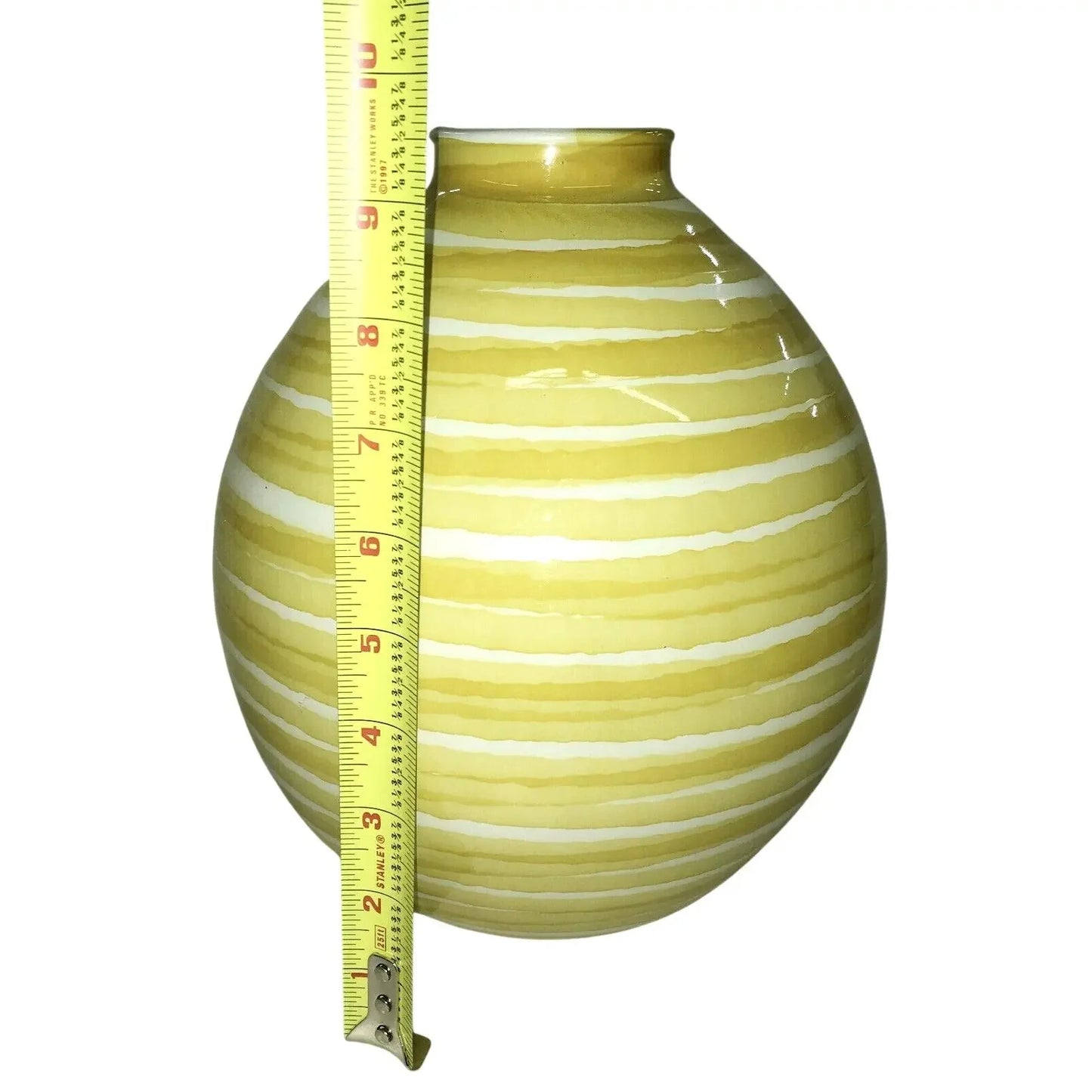 Yellow and white striped ceramic vase measured with a tape measure against a white background